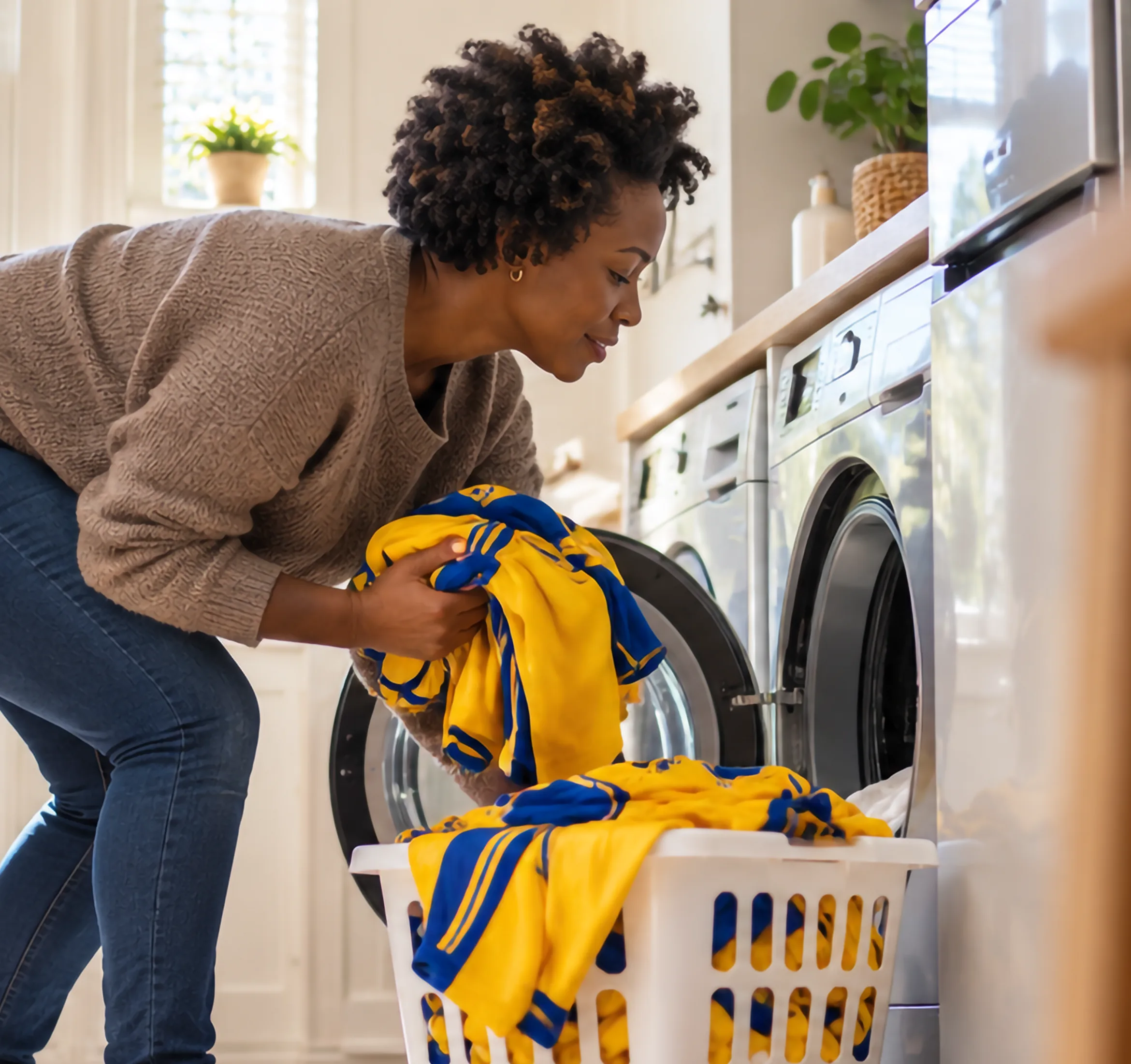 Woman taking a yellow and blue football shirt out of the washing machine in a sunny utility room
